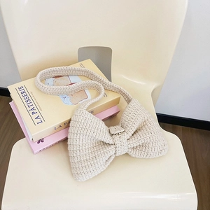 Sac à bandoulière en tricot beige avec nœud artisanal posé sur des livres colorés