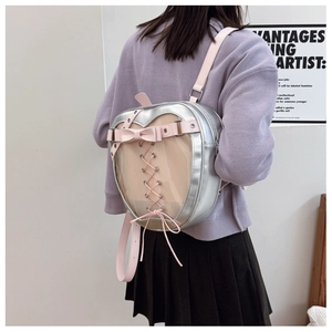 Silver heart-shaped ita bag with clear window and pink bow straps on model's back