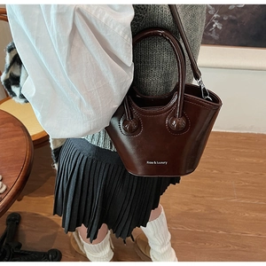 Detail of a luxury dark brown leather bucket bag with gold hardware and shoulder strap