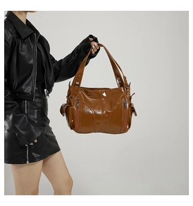 Detail of a brown oil wax leather tote bag with side pockets on a model in a leather jacket