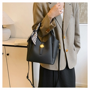 Detail of black lychee grain bucket bag with silk scarf on handle and gold hardware