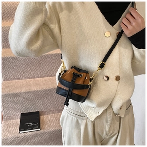 Détail du mini sac seau bicolore à cordon avec boucles dorées porté par un modèle