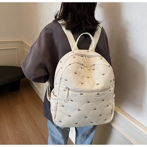 Close-up of a cream-colored quilted backpack with dark brown bow embroidery on back