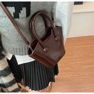 Detail of a dark brown mini bucket bag with glossy finish and Rica & Luxury text