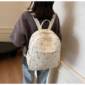 Detail of a quilted cream backpack with butterfly embroidery and front zipper pocket