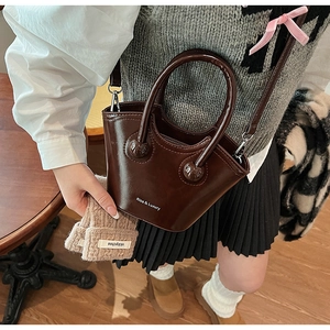Detail of a dark brown glossy leather bucket bag featuring a unique curved top handle