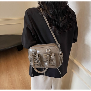 Brown vintage leather shoulder bag with bow details worn by a model in a minimalist room