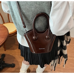 Fashionable dark brown leather bucket bag shown as a crossbody in a cozy cafe setting