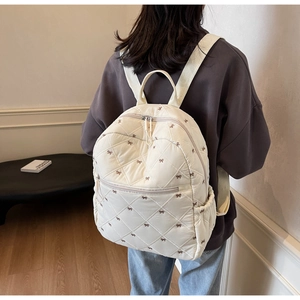 Detail of white quilted backpack featuring brown bow prints and菱格 stitching textures