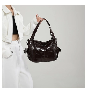 Detail of glossy dark brown PU leather hobo bag held by a model in white outfit