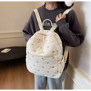 Detail of white quilted backpack featuring brown bow embroidery and sleek front zip pocket
