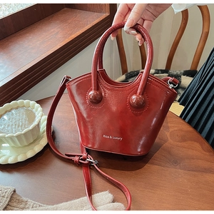 Detail view of burgundy leather bucket bag featuring gold sphere hardware and top handle