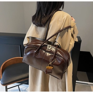 Detail of glossy dark brown PU leather handbag with gold chain and mini lock charm