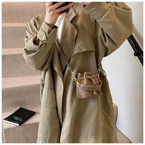 Détail d'un mini sac seau marron foncé à cordon avec chaîne dorée porté par un mannequin