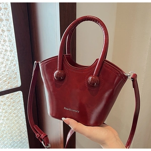 Detail of burgundy bucket bag with glossy leather texture and unique handle beads