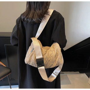 Detail of beige quilted shoulder bag with floral stitching and black nylon strap on model