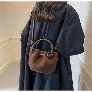 Retro dark brown suede bucket bag with leather knot handle detail on a black coat