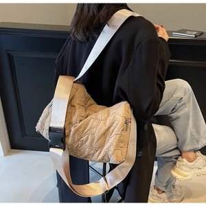Detailed shot of beige quilted floral crossbody bag with wide strap and zip closure