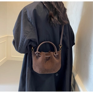 Brown faux suede bucket bag shown from behind on a model wearing a navy blue winter coat