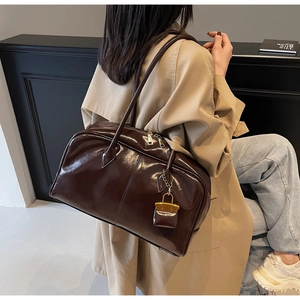 Detail of a dark brown glossy leather Boston bag with gold zippers worn by a model