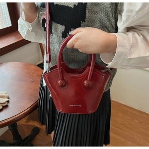 Close-up of red glossy bucket bag featuring unique spherical handle hardware and logo