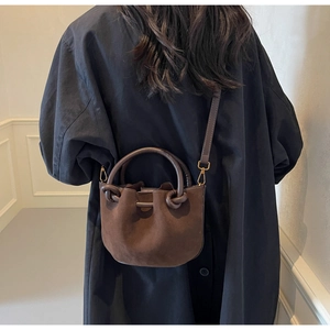 Detail of dark brown faux suede bucket bag with knot design and detachable strap on model
