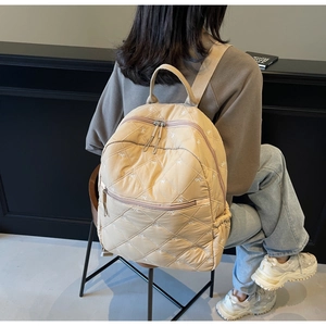 Detail of beige quilted backpack with bow embroidery and sleek nylon texture on model