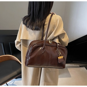 Detail shot of a dark brown patent leather shoulder bag with a stylish mini charm accessory