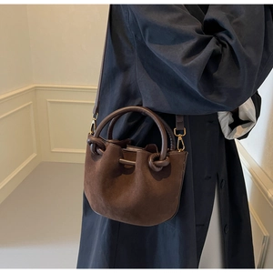 Detailed shot of dark brown suede bucket bag with knotted handle on a navy blue coat