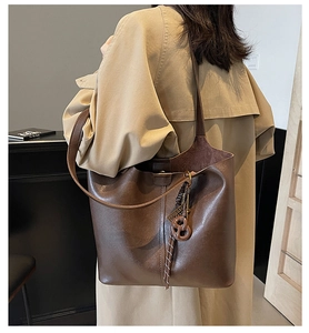 Detail of dark brown matte leather tote bag with knot charm on model in trench coat