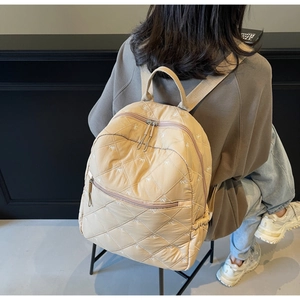Detail of beige quilted backpack showing diamond stitching and white bow embroidery