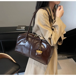 Detail view of dark brown glossy Boston handbag with golden lock charm and dual straps