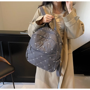 Detail showing grey quilted backpack with white bow prints and diamond stitching texture