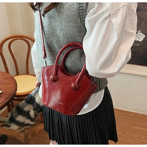 Detail view of burgundy glossy leather handbag with gold logo and round handle accents