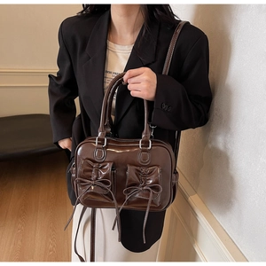 Detail view of dark brown patent leather boston bag with decorative bow front pockets