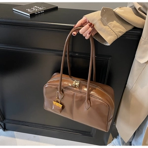 Detail of dark brown glossy PU leather Boston bag with gold zipper and metal lock charm