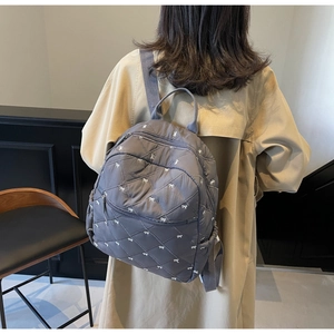 Close-up of gray quilted backpack with embroidered bows on a model in a beige coat