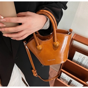 Detail of caramel brown leather bucket bag showing circular handle joint and adjustable strap