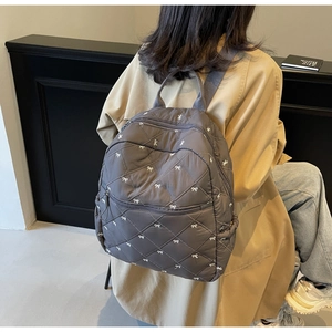 Detail of grey quilted backpack with white bows and diamond stitching on fabric