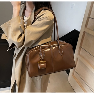 Detail of brown glossy patent leather shoulder bag with a mini decorative charm