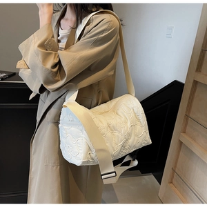 Detail of white quilted messenger bag featuring floral embroidery and wide fabric strap