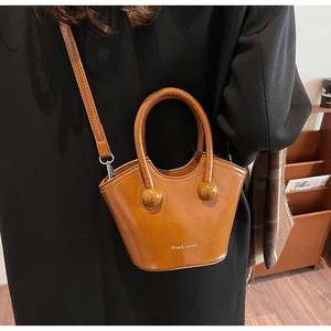 Detail of caramel leather bucket bag with top handle and brand logo on a black coat background