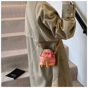 Détail du sac seau rose à cordon avec bordure en cuir marron porté sur un trench-coat beige