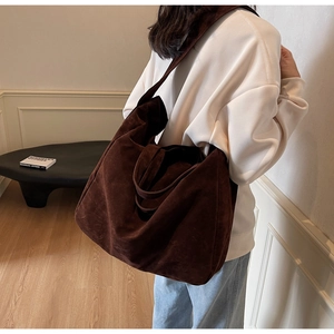 Detail view of deep brown suede tote bag carried by a model in a minimalist room