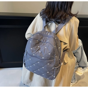 Close-up of diamond quilted gray backpack featuring white bow embroidery and front pocket
