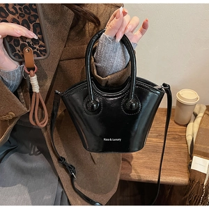 Detail of black glossy bucket bag with spherical handle ornaments and brand logo