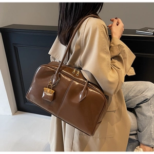 Detail of brown PU leather shoulder bag with gold hardware and padlock pendant on a model