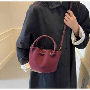 Burgundy faux suede bucket bag with drawstring details on a navy trench coat