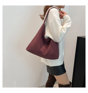 Dettaglio di una borsa hobo bordeaux scuro indossata da una modella in interni semplici