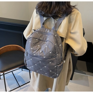 Quilted gray backpack with white bow patterns worn by a person in a minimalist interior